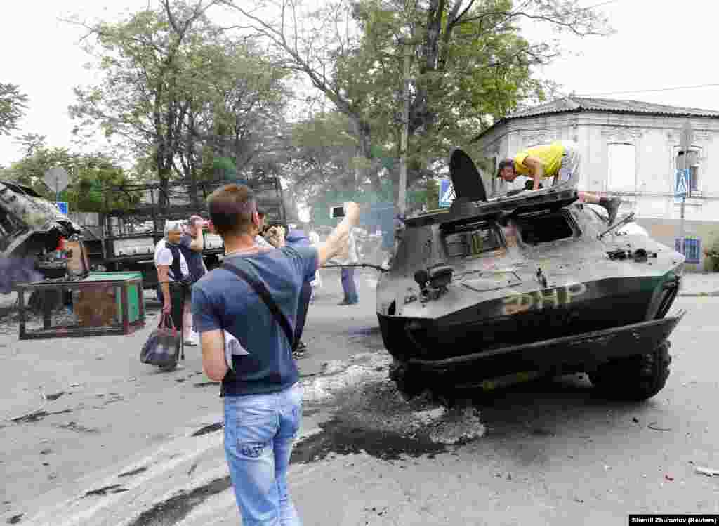 Местные жители фотографируют уничтоженный бронетранспортер, который принадлежал контролируемым Россией силам, захватившим в городе административные здания. Мариуполь, 13 июня