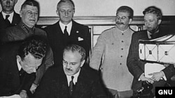 Вячеслав Молотов подписывает знаменитый пакт о ненападении. Позади него - Риббентроп и Сталин
