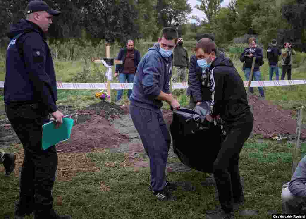Policajac gleda kako muškarci nose tijelo osobe koju su, prema ukrajinskoj policiji, ubile ruske trupe u Balakliji.