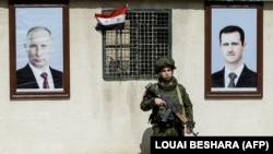 Ruski vojnik stoji između portreta sirijskog predsjednika Bashara al-Assada (desno) i ruskog predsjednika Vladimira Putina na kontrolnom punktu na periferiji Damaska, 2018. godine.