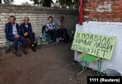 Stanovnici sjede blizu skloništa gdje su se skrivali tokom sukoba ukrajinskih i ruskih snaga u Kurskoj oblasti u Rusiji. Na plakatu piše: "Civili u podrumu, nema vojnika."